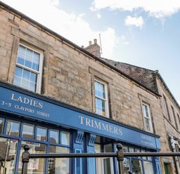 A stone building with blue storefront signage for ladies and gents trimmers at 3-5 Clayport Street at 1 Pringles Yard in Alnwick