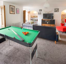 A living room with a pool table a black sofa a red armchair and a television at 1 Pringles Yard in Alnwick