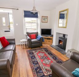 A sitting room with leather sofas a patterned rug a wood burning stove and a television at Victoria Cottage in Chipping Norton