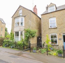 Stone cottages with gardens and black metal fences on a street at Victoria Cottage in Chipping Norton