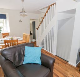 A living room with a dark leather chair and blue cushion next to a wooden dining table with six chairs and tableware at Victoria Cottage in Chipping Norton