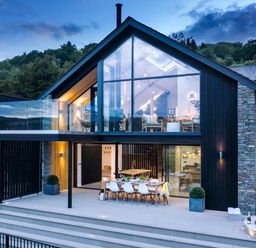 A modern two-story house with large glass windows a dining table on the patio and a hot tub outside at Gatesgarth in Coniston