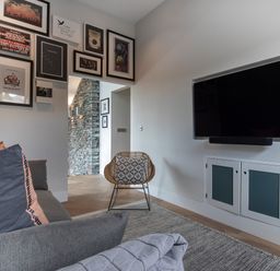 A living room with a gray sofa and pillows a wicker chair a wall-mounted television and framed pictures above a doorway at Gatesgarth in Coniston