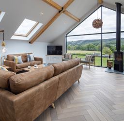 A living room with leather sofas a wood stove and large windows overlooking a green landscape at Gatesgarth in Coniston
