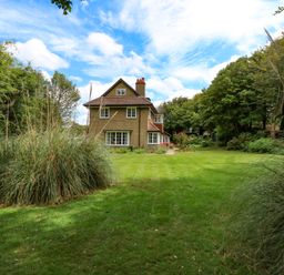 A house with a tiled roof surrounded by grass and trees at Beckhythe Cottage in Overstrand