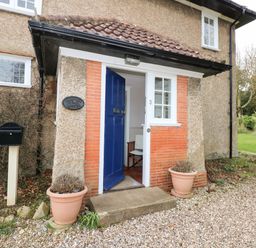 A blue door entrance of a house with two flower pots and a black mailbox at Beckhythe Cottage in Overstrand