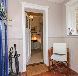 An entryway with a blue door a wooden chair with white fabric an umbrella stand and a doormat at Beckhythe Cottage in Overstrand