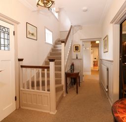 A hallway with stairs a small wooden table framed pictures and a door with decorative glass panels at Beckhythe Cottage in Overstrand