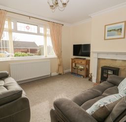 A living room with two sofas a TV on a wooden stand a fireplace and a large window with curtains at Arbour Retreat in Filey