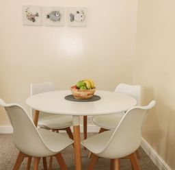 A round white dining table with four white chairs and a bowl of fruit on top with fish artwork on the wall at Arbour Retreat in Filey