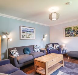 A living room with sofas cushions wooden coffee table and paintings at Silver Birch Lodge in Ratagan Glenshiel near Dornie