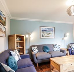 A living room with three blue sofas a wooden coffee table a wooden shelf lamps and landscape paintings at Silver Birch Lodge in Ratagan Glenshiel near Dornie