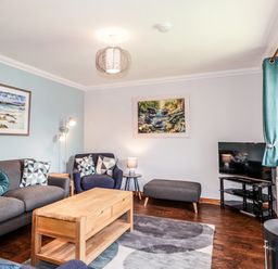 A living room with a grey sofa and armchair a wooden coffee table a television on a stand and framed paintings on the walls at Silver Birch Lodge in Ratagan Glenshiel near Dornie