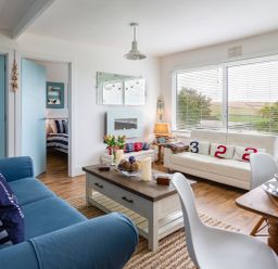 A living room with blue and white sofas a wooden coffee table white chairs and a dining table at The Hut in Dartmouth