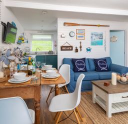 A dining and living area with a wooden table set for four and a blue sofa with cushions at The Hut in Dartmouth