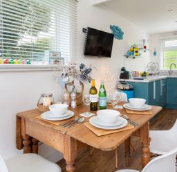A dining area with a wooden table set with bowls and glasses next to a kitchen with blue cabinets at The Hut in Dartmouth