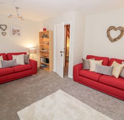 A living room with two red sofas and a wooden bookshelf with decorative items at Valentines Cottage in Stratford-Upon-Avon