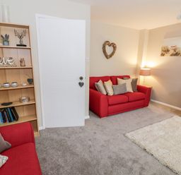 A living room with red sofas a wooden bookshelf a lamp a rug and wall decorations at Valentines Cottage Stratford-Upon-Avon