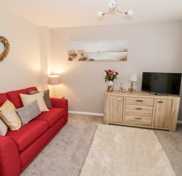 A living room with a red sofa pillows a wooden cabinet a television and decorative items at Valentines Cottage Stratford-Upon-Avon
