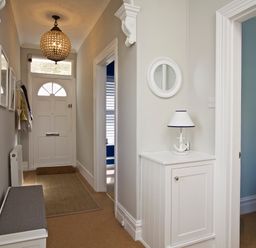 A hallway with a white front door a bench a white cabinet with a lamp and an open doorway at Armorel House in Dartmouth