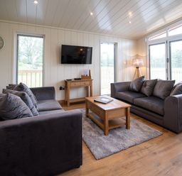 A living room with two sofas a wooden coffee table a wall clock and a television at Otter Lodge in Gargrave