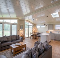 An open living room and kitchen area with sofas a coffee table dining table and kitchen island at Otter Lodge in Gargrave