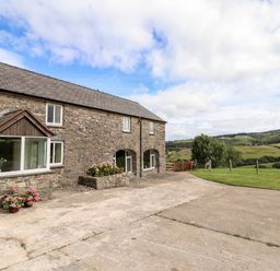 An exterior view of a stone building with windows and flower pots next to a concrete driveway and green fields at The Stables At Cae Gwyn in Ruthin