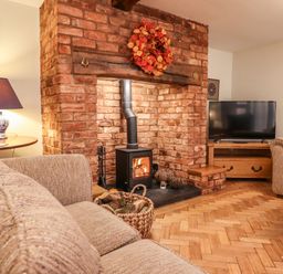A living room with brick fireplace wood stove beige sofas television and wooden furniture at The Stables At Cae Gwyn in Ruthin