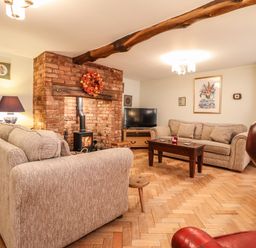 A living room with two beige sofas a brick fireplace with a wood stove a wooden coffee table and a television at The Stables At Cae Gwyn in Ruthin
