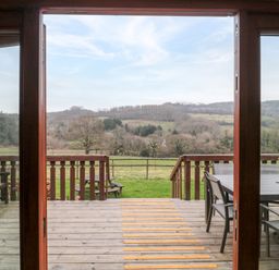 A wooden deck with outdoor furniture and a view of fields and hills at The Willow Lodge near Lyme Regis