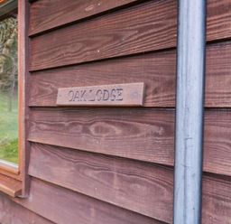 A wooden exterior wall with a small sign reading oak lodge and a window showing trees outside at The Oak Lodge near Lyme Regis