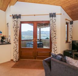 A living room with a sofa a television and glass doors leading to a balcony at The Oak Lodge near Lyme Regis