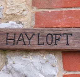 A wooden sign engraved with the words HAY LOFT mounted on a stone and brick wall at The Hayloft Cottage Apartment near Lyme Regis