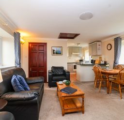 A living room with black leather sofa and armchair a wooden coffee table and dining table with chairs at The Hayloft Cottage Apartment near Lyme Regis