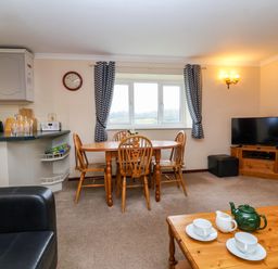 A living room with a wooden dining table and chairs a tv on a wooden stand and a coffee table with a teapot and cups at The Hayloft Cottage Apartment near Lyme Regis