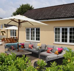 An outdoor patio with sofas, a table, umbrellas, and a dining area at The Anchorage @ Nables Farm in Upper Seagry
