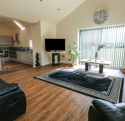 A living room with a black rug a coffee table with flowers a wall clock a TV and an open kitchen at Ty Cuddfan in Llangoed