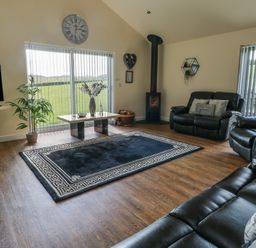 A living room with black leather sofas a rug a coffee table a wood stove and windows with vertical blinds at Ty Cuddfan in Llangoed