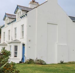 A white two-story house with blue trim and a blue door with plants and grass in the foreground at Carriguisnagh in Ballycastle