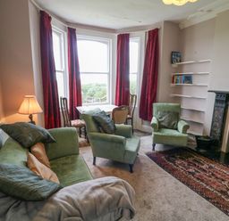 A living room with green sofas a wood burning stove and red curtains at Carriguisnagh in Ballycastle