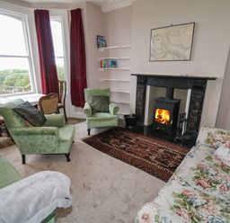 A living room with green armchairs floral sofa wood stove and red curtains at Carriguisnagh Ballycastle