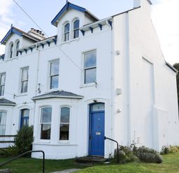 A white two-story house with blue doors and windows surrounded by grass at Carriguisnagh in Ballycastle