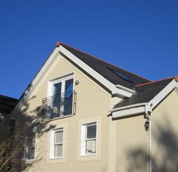 A two-story house with beige walls white window frames and a black roof under a clear blue sky at Monterey Mews in Torquay