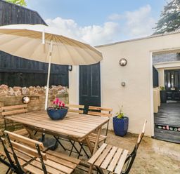 An outdoor patio with a wooden table and chairs under a large umbrella at Monterey Mews in Torquay