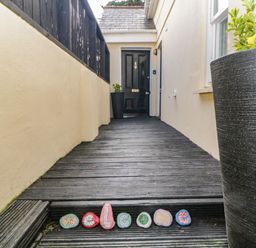A front porch with a black door wooden decking and painted stones spelling welcome at Monterey Mews in Torquay