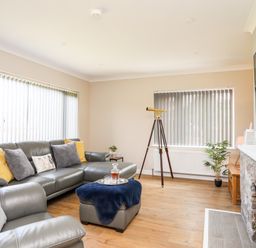 A living room with a grey leather sofa and armchair a telescope and a stone fireplace at Little Mead in Trearddur Bay