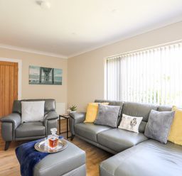 A living room with grey leather sofas and yellow and grey cushions at Little Mead in Trearddur Bay