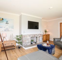 A living room with a wall-mounted TV fireplace wooden cabinets telescope and gray leather furniture at Little Mead in Trearddur Bay