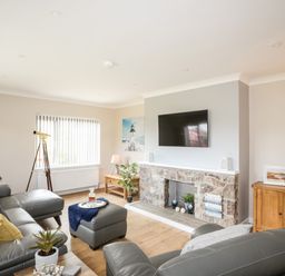 A living room with gray leather sofas a stone fireplace and a wall-mounted TV at Little Mead in Trearddur Bay