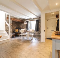 A dining area with a round table and white chairs next to a stone wall with a built-in seating area and stairs in Awelfa Newport Pembrokeshire